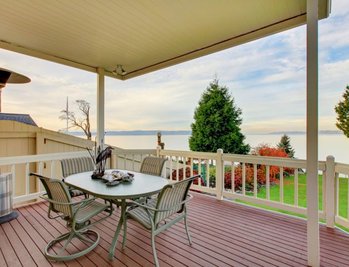 An elegant waterfront patio dining area with a round table set for four, overlooking a stunning view of the ocean under a clear sky.